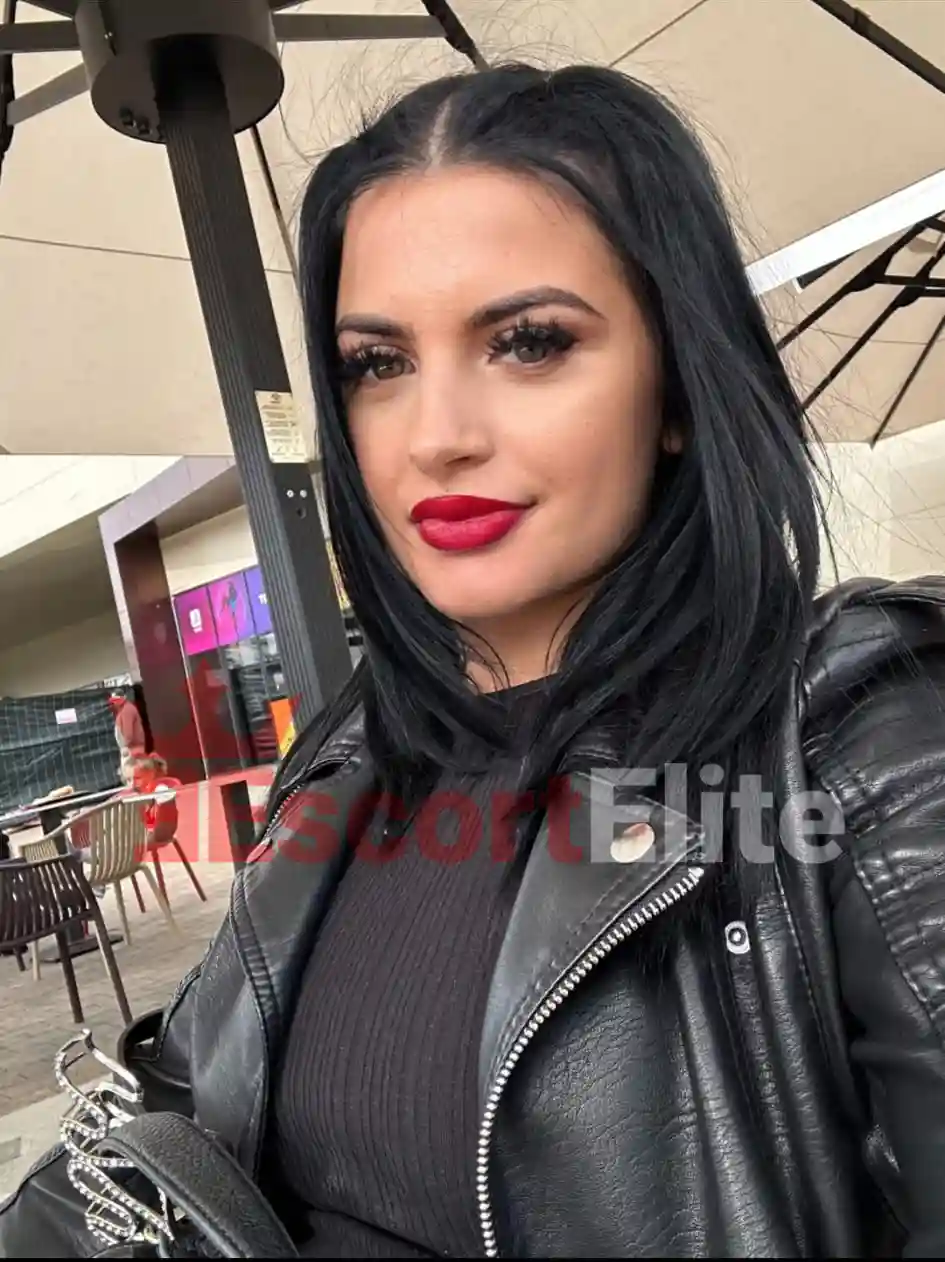 Alessia Premium Escort Wien Nahaufnahme-Selfie in schwarzer Lederjacke mit roten Lippen auf einer Caféterrasse