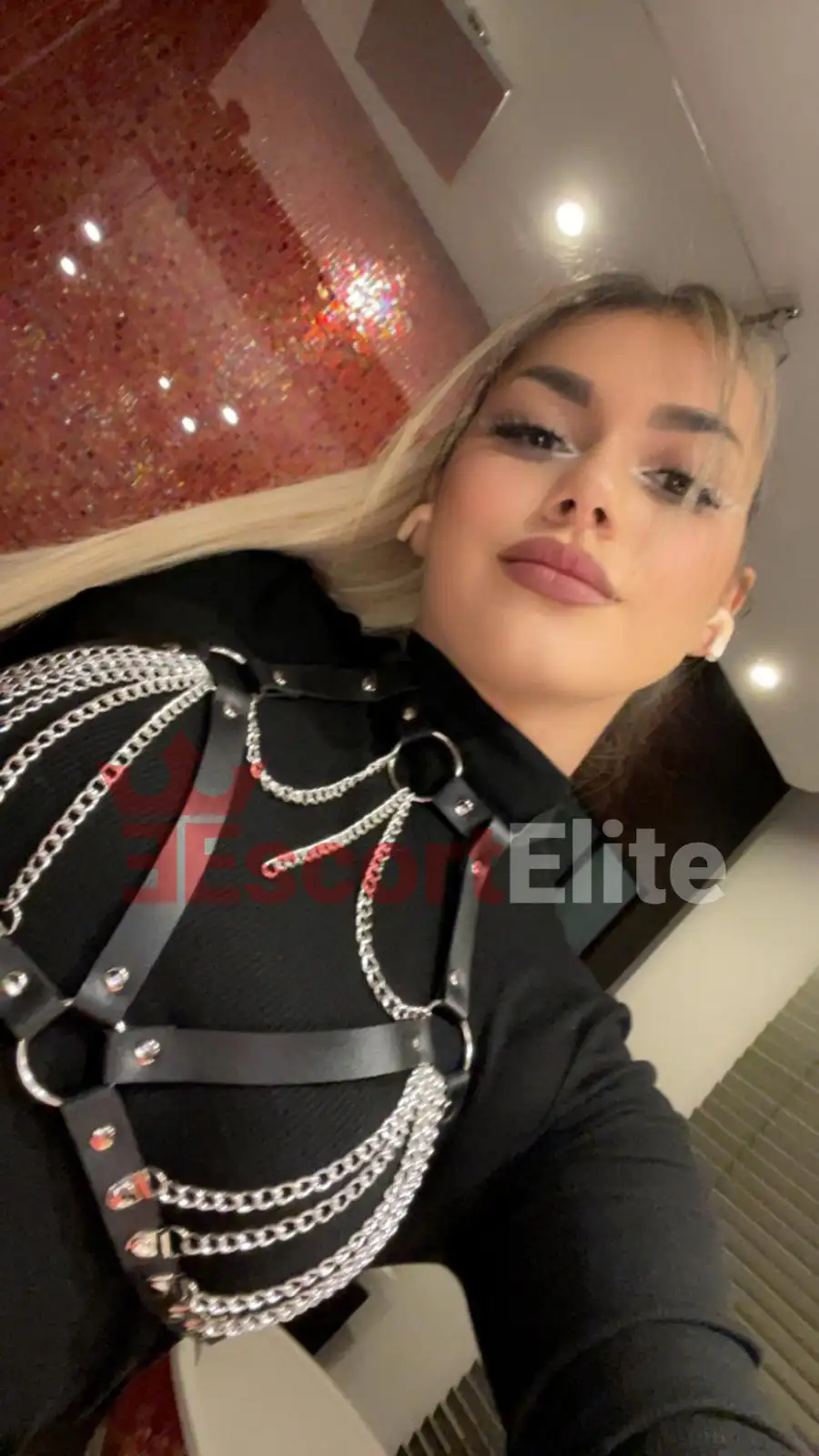 Jasmin Escort Wien – Harness & Ketten Blonde Escort Wien Jasmin mit schwarzem Leder-Harness und Silberketten, glamouröses Porträt