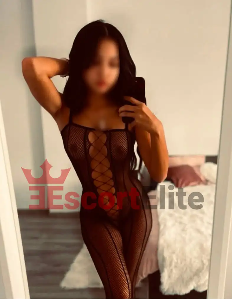 Mely Wien – Sinnliches Netz-Catsuit Portrait Junge Escort Mely Wien im schwarzen Netz-Catsuit mit erhobenem Arm im Haar, sinnliches Portrait im Schlafzimmer